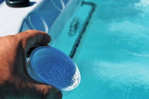 Person holding a scoop of spa chemicals over hot tub water.
