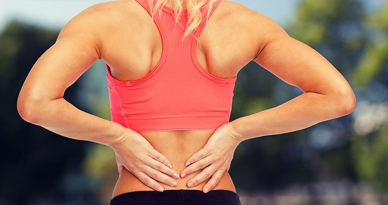 Person holding lower back while standing outdoors