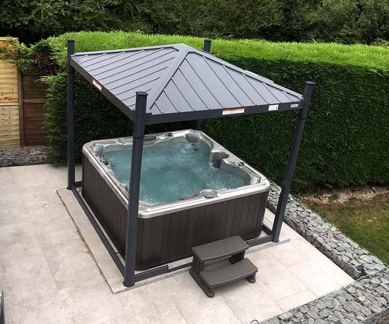 Hot tub under a metal gazebo in a landscaped backyard.