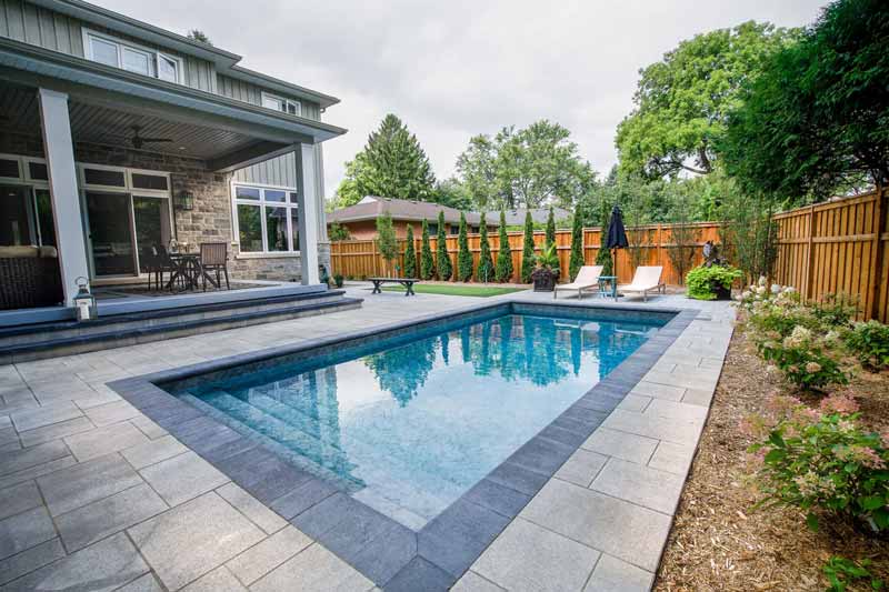 Backyard rectangular pool beside a patio and garden.