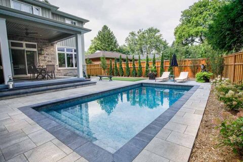 Backyard rectangular pool beside a patio and garden.