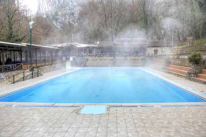 Steam rising from an outdoor pool surrounded by trees and seating.