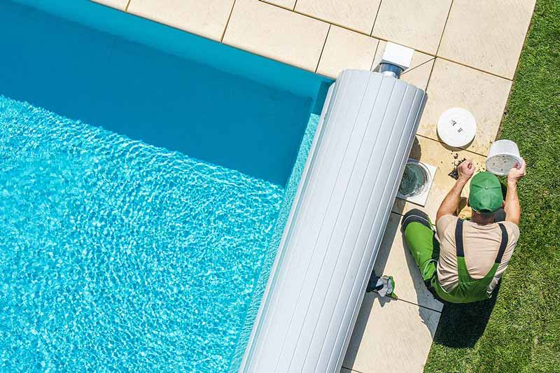 Person performing pool maintenance beside a swimming pool with a cover roller