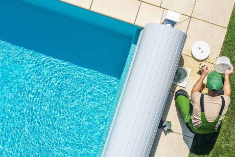 Person performing pool maintenance beside a swimming pool with a cover roller