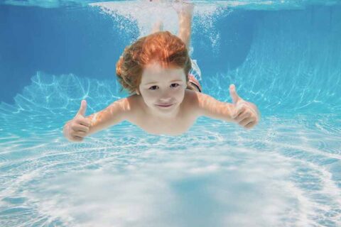 Child swimming underwater giving thumbs up