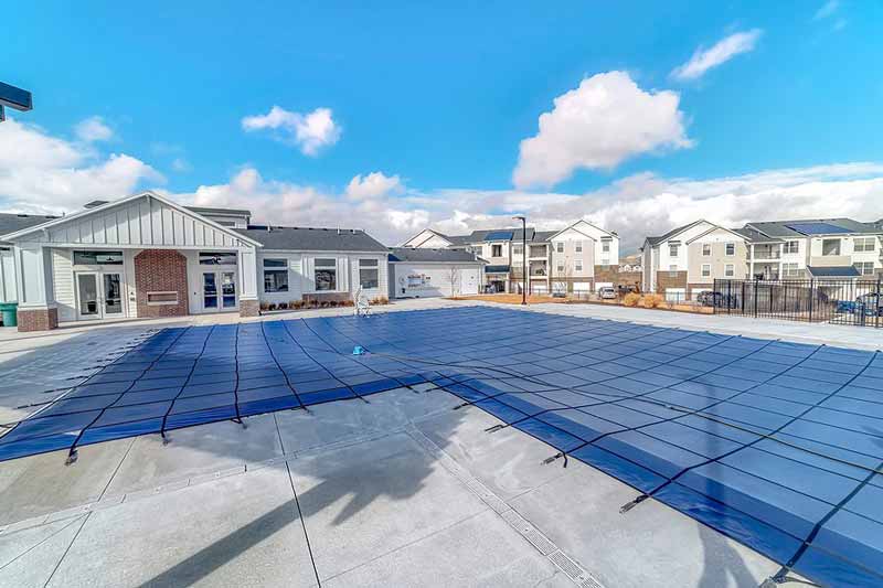 Outdoor swimming pool covered with a blue safety cover in a residential area.”